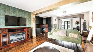 A living room with a flat-screen TV, wooden flooring, a green sofa, and a fireplace.