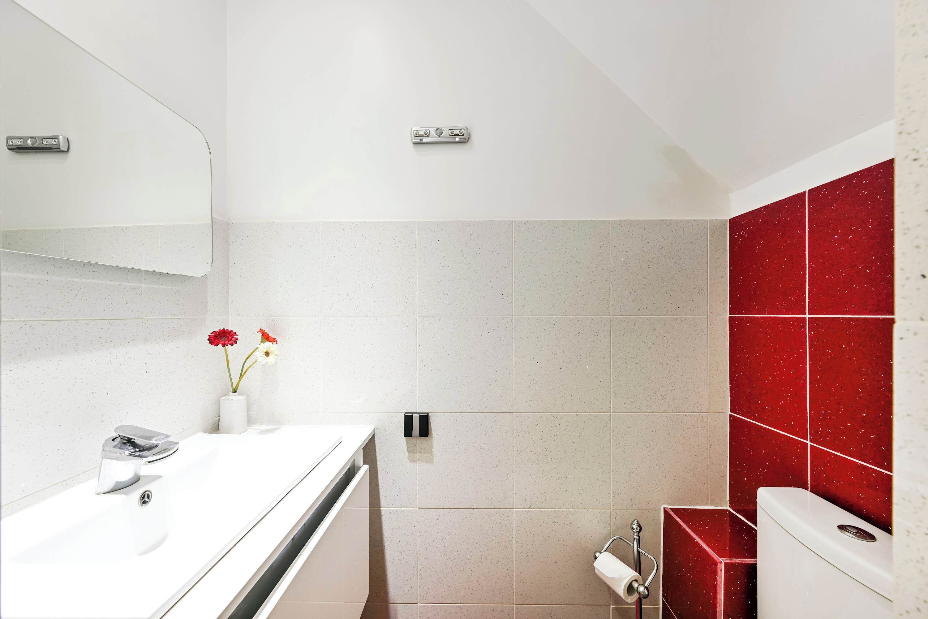 A bathroom with a white sink, mirror, and red-tiled shower area.