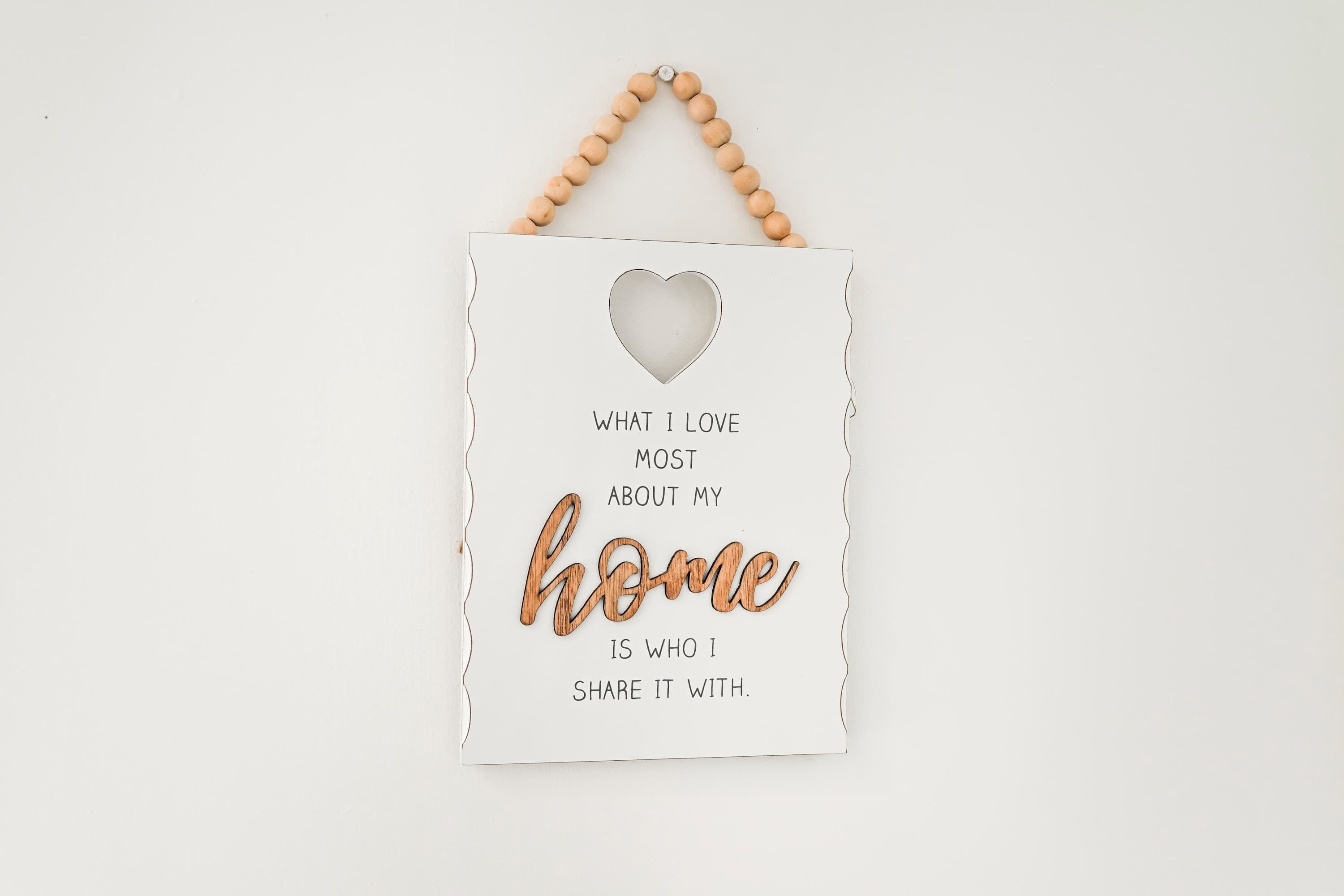 Une plaque blanche ornée d’un cœur en bois découpé, sur laquelle on peut lire : « Ce que j’aime le plus dans ma maison, ce sont les personnes avec qui je la partage. »