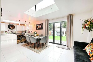 A modern kitchen with a central island, dining area with chairs, and a large sliding glass door leading to a patio. - Windsor 5-Bed House - Near Castle - Sleeps 13 (Greater London)