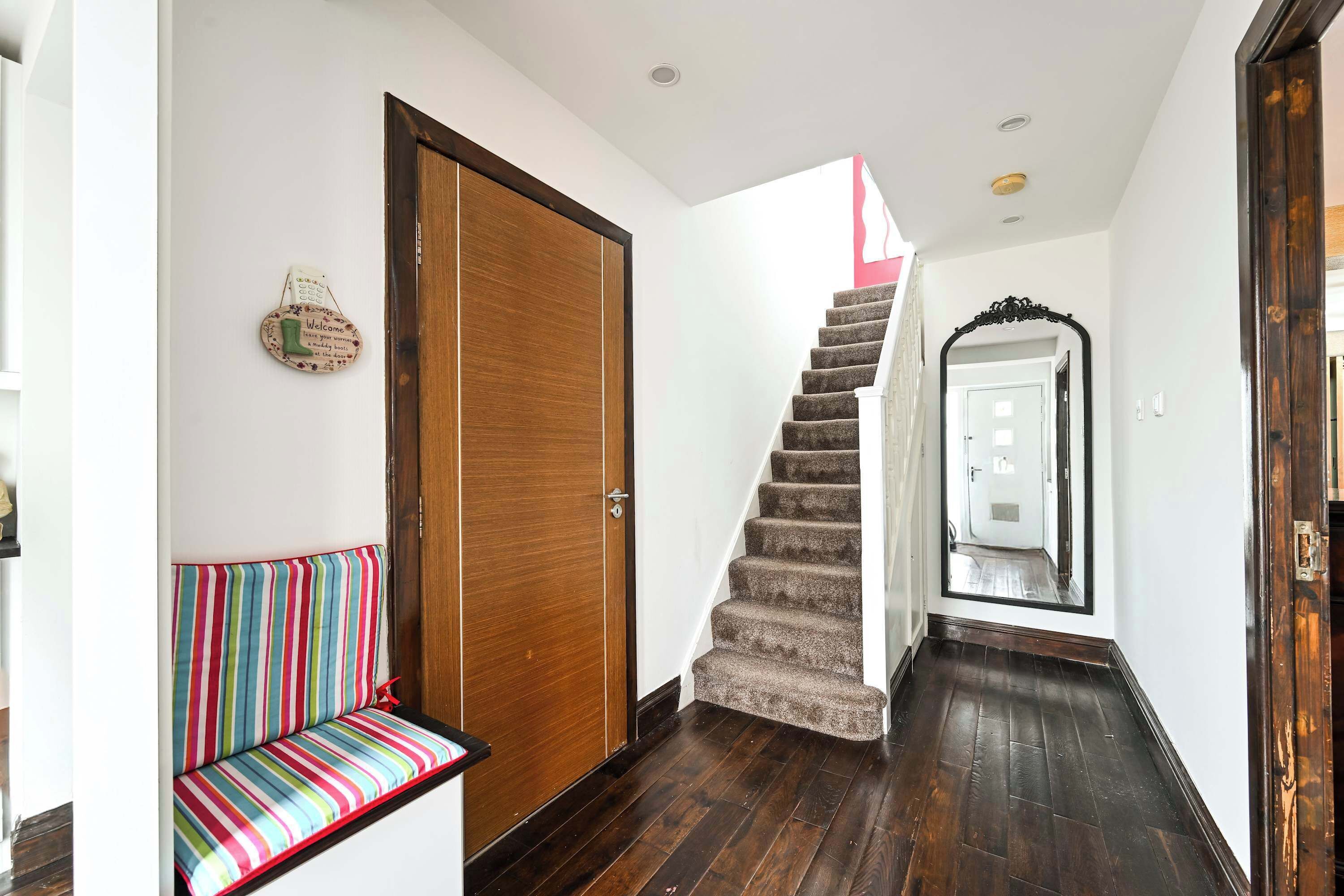 A hallway with a wooden door, a striped bench, and a carpeted staircase leading to another room.