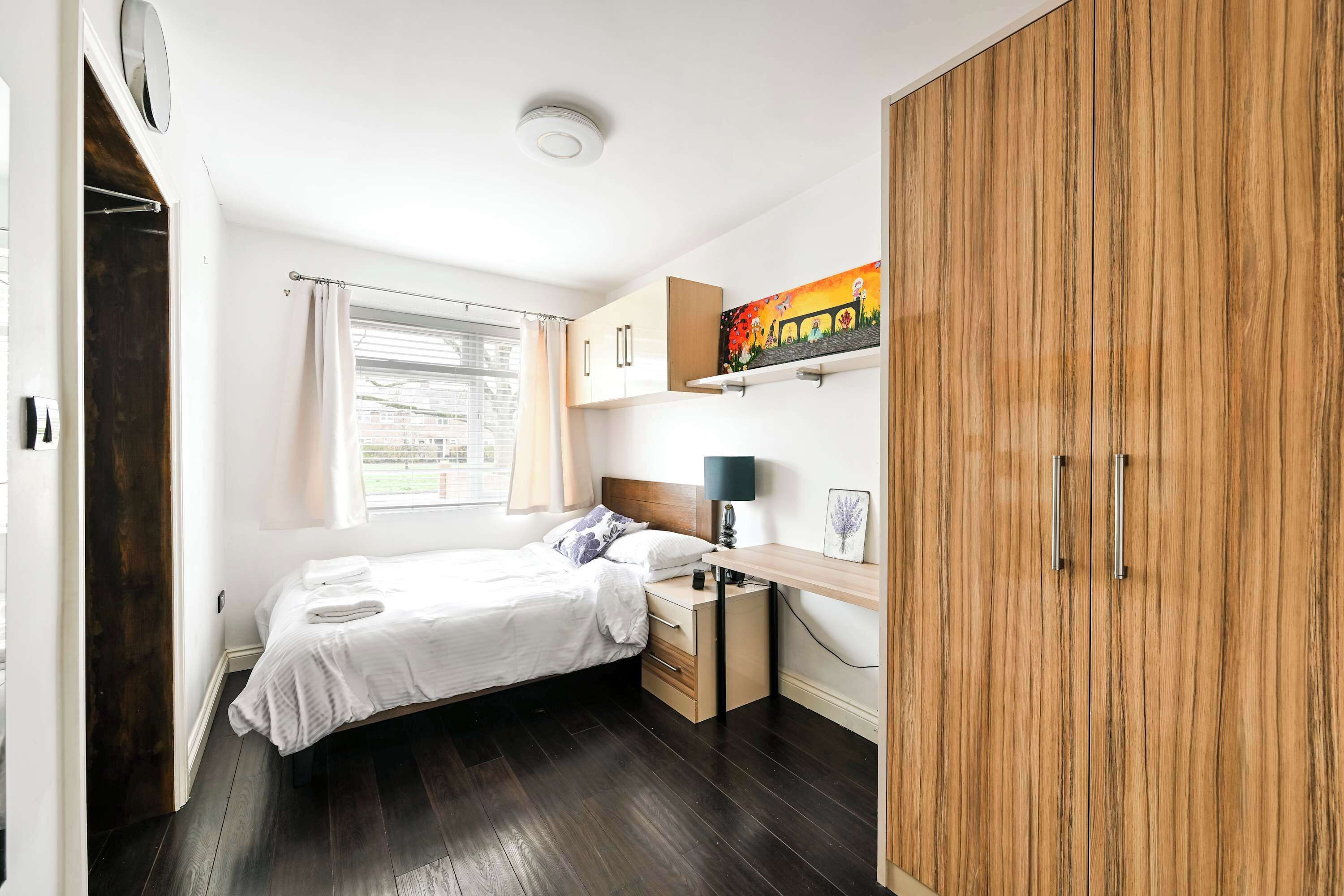 A bedroom with a bed, a desk, a wardrobe, and a window with curtains.
