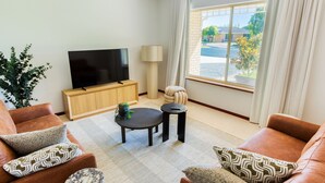 Een moderne woonkamer met een flatscreen televisie, een houten kast en een groot raam met gordijnen.