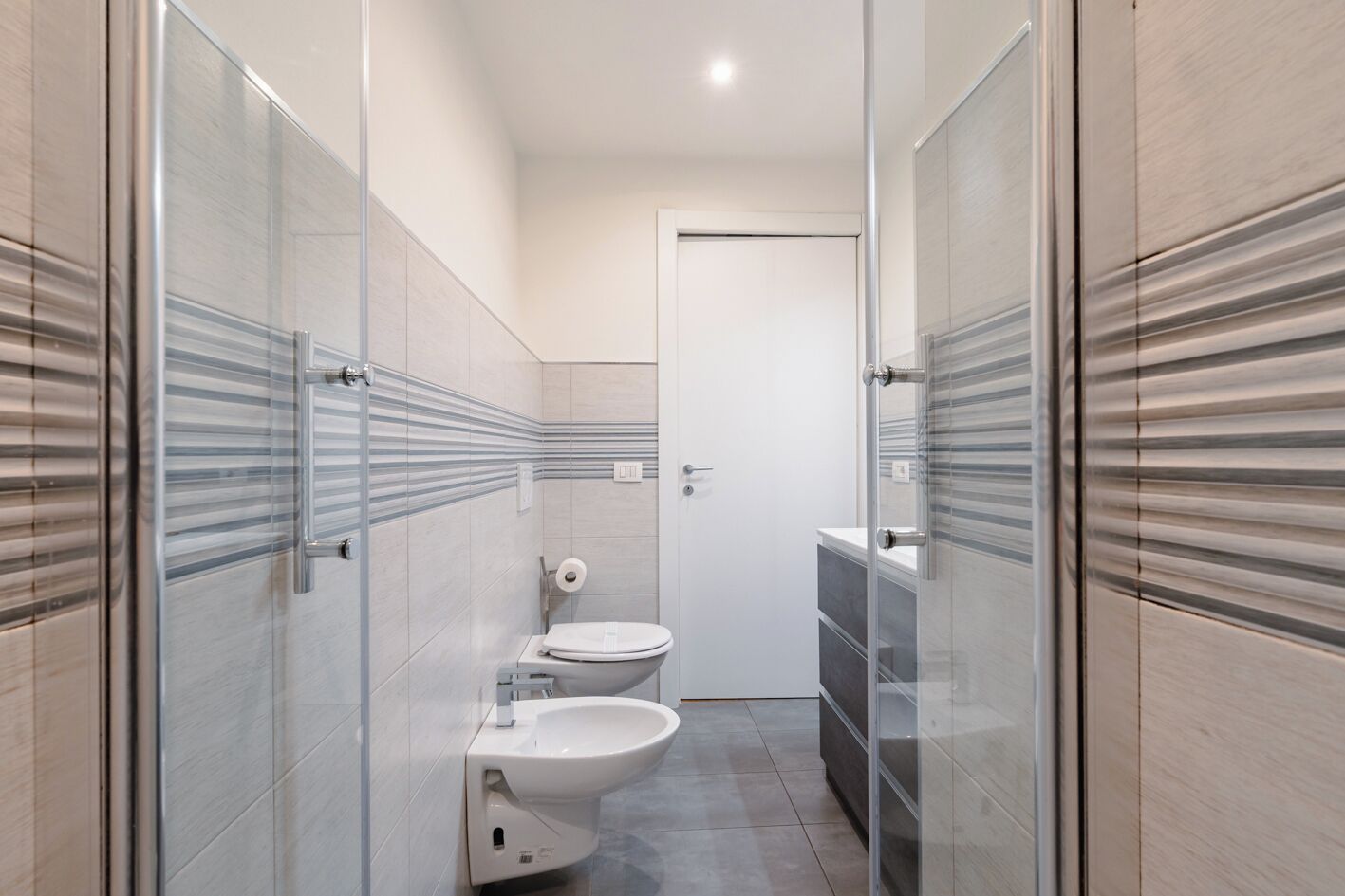 Ein schmales Badezimmer mit Toilette, Bidet und einer Duschkabine aus Glas.
