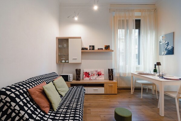 A modern living room with a sofa, a dining table, and a kitchen area. - Aurora Urban Nest (Firenze)