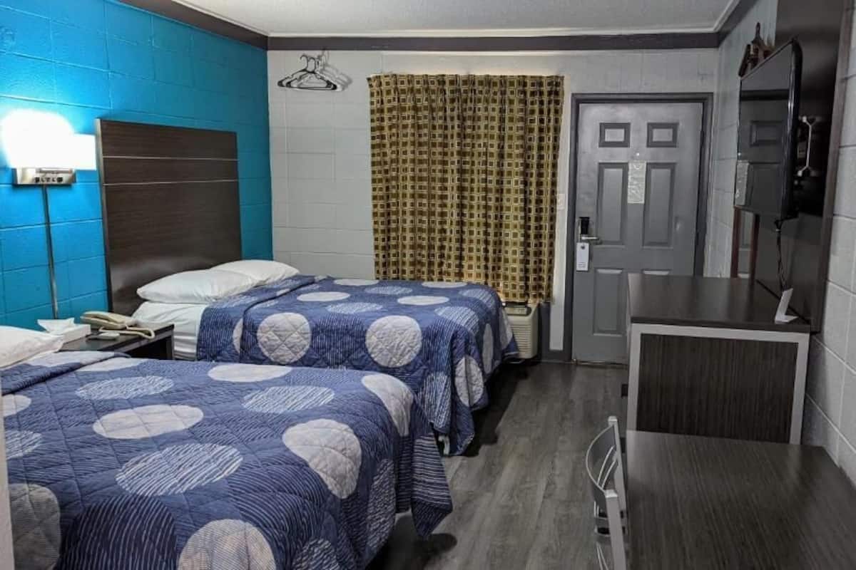 Hotellihuone, jossa on kaksi sänkyä, työpöytä, televisio ja suihku.