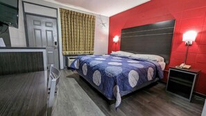 A bedroom with a bed, a desk, a chair, a red wall, and a window with curtains. - sheridan inn (Sheridan)