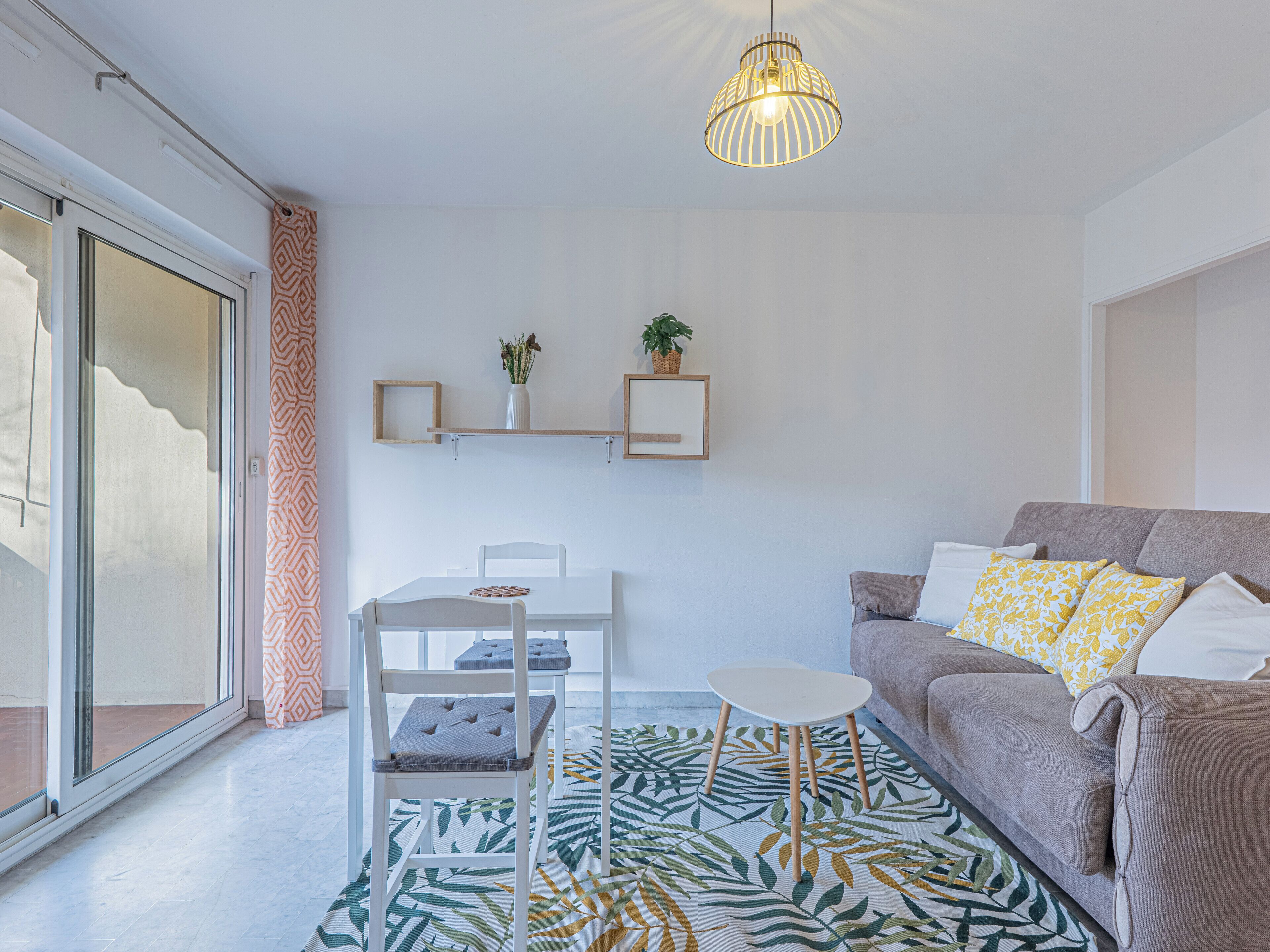 A modern living room with a sofa, a dining table, and a hanging light fixture.