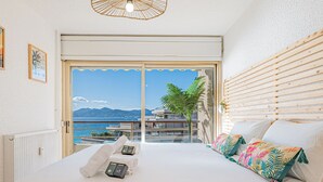 A bedroom with a large bed, a view of the sea, and a balcony with wooden blinds. - Elégant 2 pièces - accès mer direct vue splendide (Cannes)