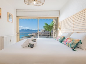 Ein Schlafzimmer mit großem Bett, Meerblick und einem Balkon mit Holzjalousien.