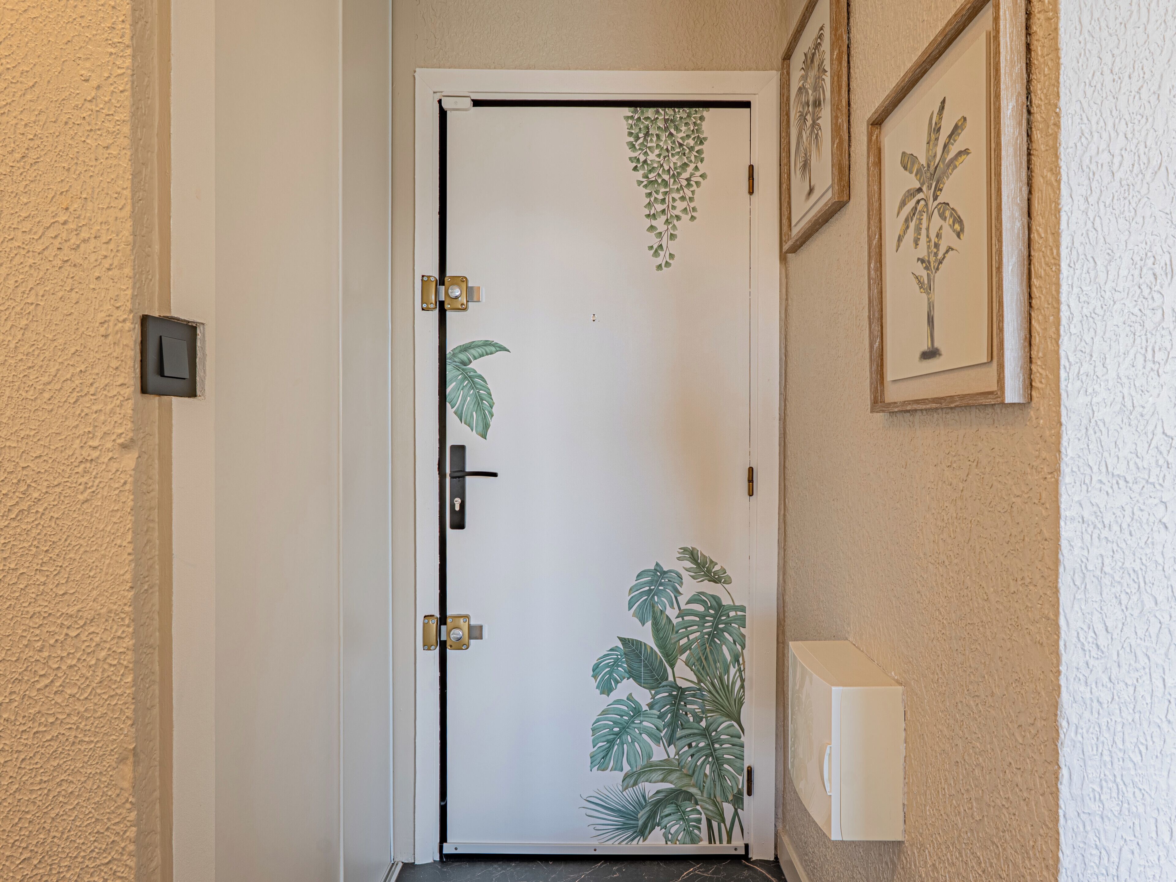 Une porte ornée d’un motif végétal, un interrupteur et un tableau encadré accroché au mur.