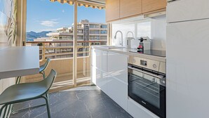 A modern kitchen with a view of a coastal building, a dining area with a table and chairs, and a large window with a view of the sea. - Elégant 2 pièces - accès mer direct vue splendide (Cannes)