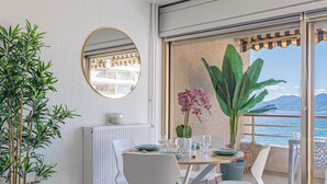 A balcony with a dining table set for two, a potted plant, and a view of the sea. - Elégant 2 pièces - accès mer direct vue splendide (Cannes)
