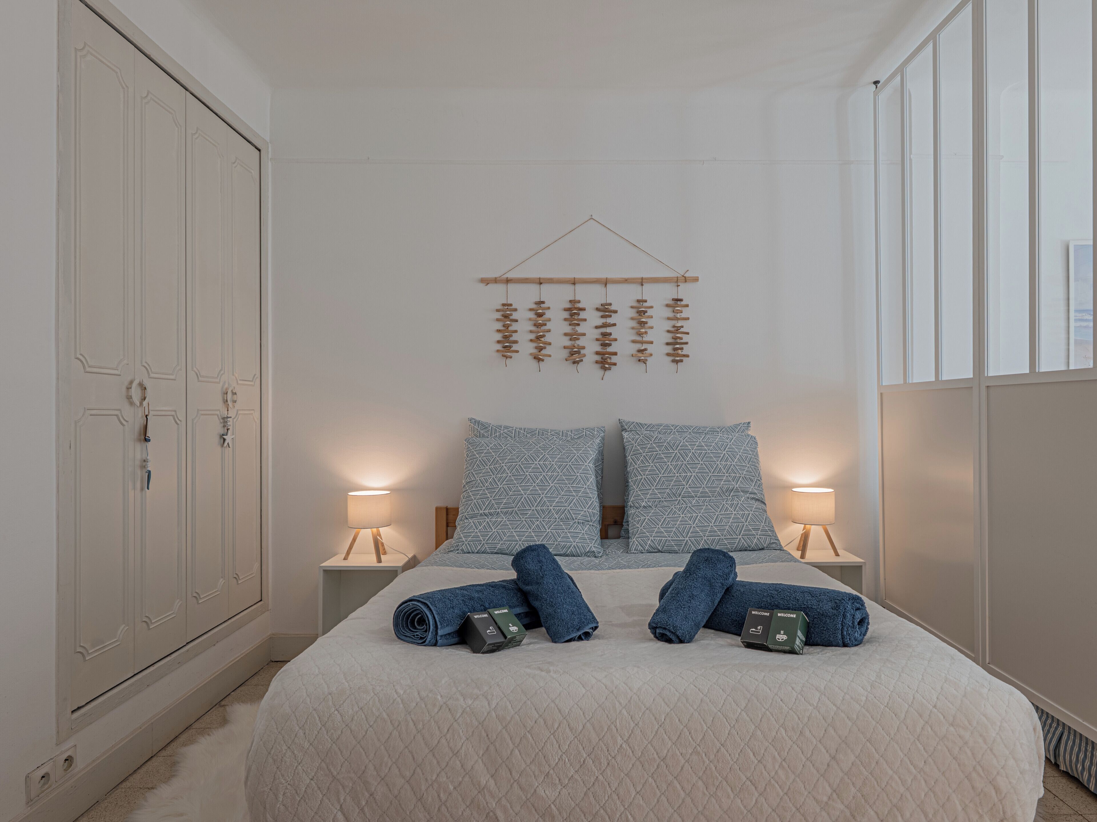 A hotel room with a large bed, two bedside tables, a wardrobe, and a wall-mounted hanging decoration.