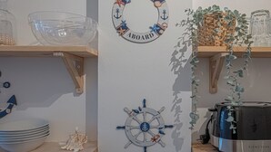 Paredes com um letreiro de boas-vindas com tema náutico, um leme decorativo e prateleiras com tigelas e uma planta.