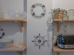 A wall with a nautical-themed welcome sign, a ship's wheel decoration, and shelves with bowls and a plant. - Le Bleu Ciel - Studio Croisette idéal congrès (Cannes)