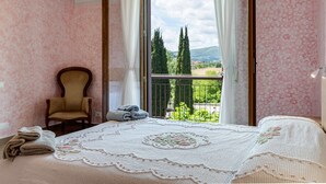 A bedroom with a bed, a chair, a balcony with a view of trees and hills.
