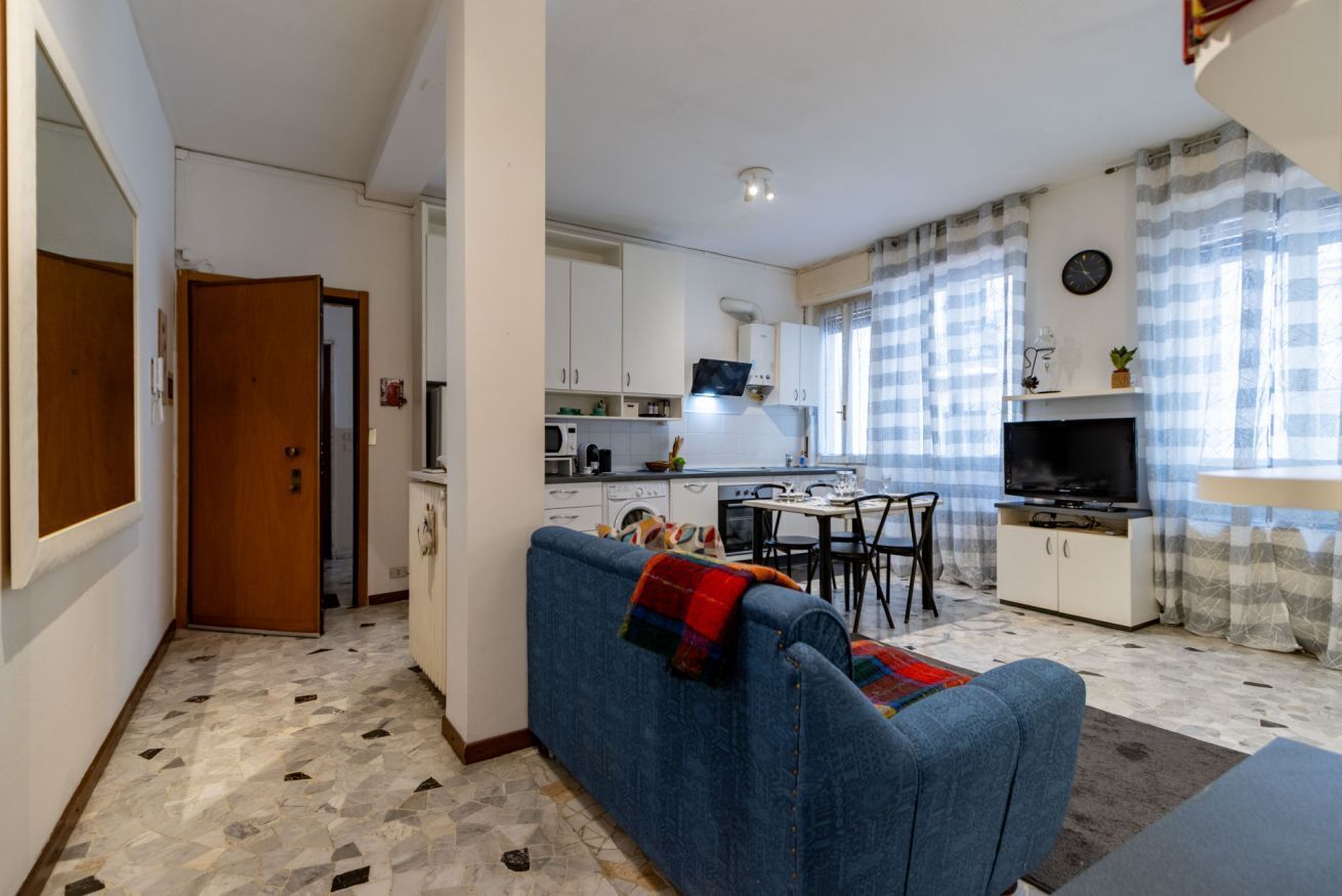 Un ambiente compatto con angolo cottura, divano, tavolo da pranzo e televisione.
