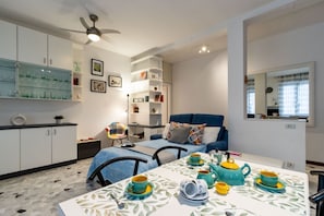 Ein gemütlicher Wohnbereich mit Küchenzeile, einer Essecke mit für Tee gedecktem Tisch, einem blauen Sofa und einem Deckenventilator.