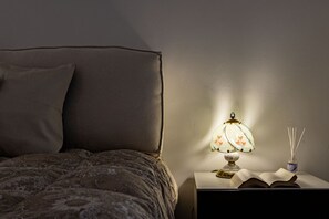 Un letto con una coperta a motivi, una lampada da comodino con un disegno floreale e un libro aperto su un tavolino.