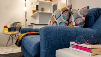 Ein blaues Sofa mit gemustertem Bezug, ein Stapel Bücher und eine Brille auf einem weißen Hocker.