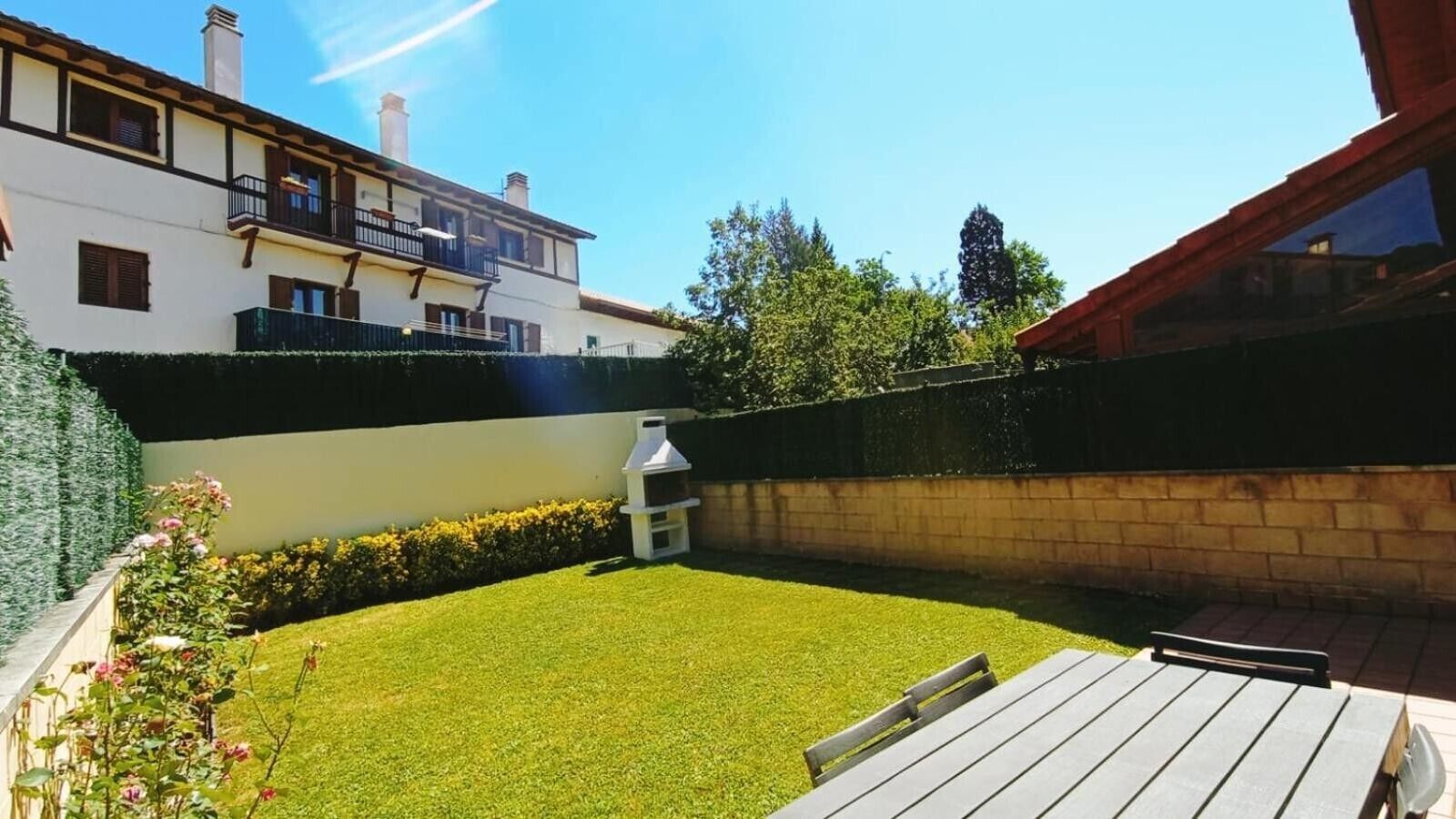 Un patio trasero con terraza de madera, una parrilla y césped bien cuidado.