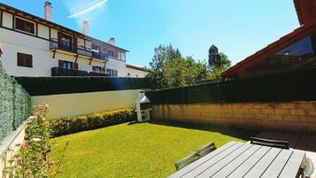 Un patio trasero con terraza de madera, una parrilla y césped bien cuidado.