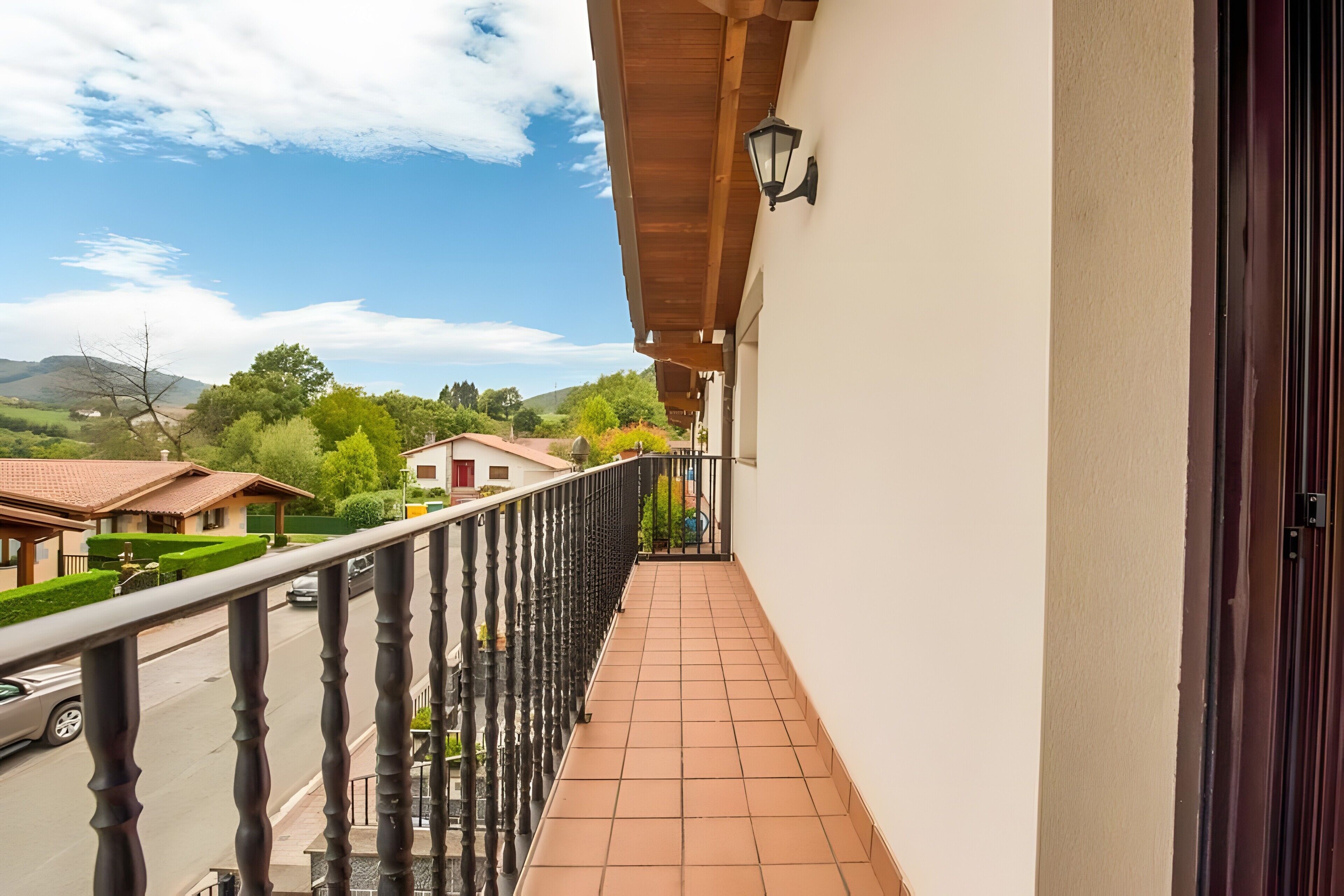 A balcony with a tiled floor, a black railing, and a view of a street and greenery.