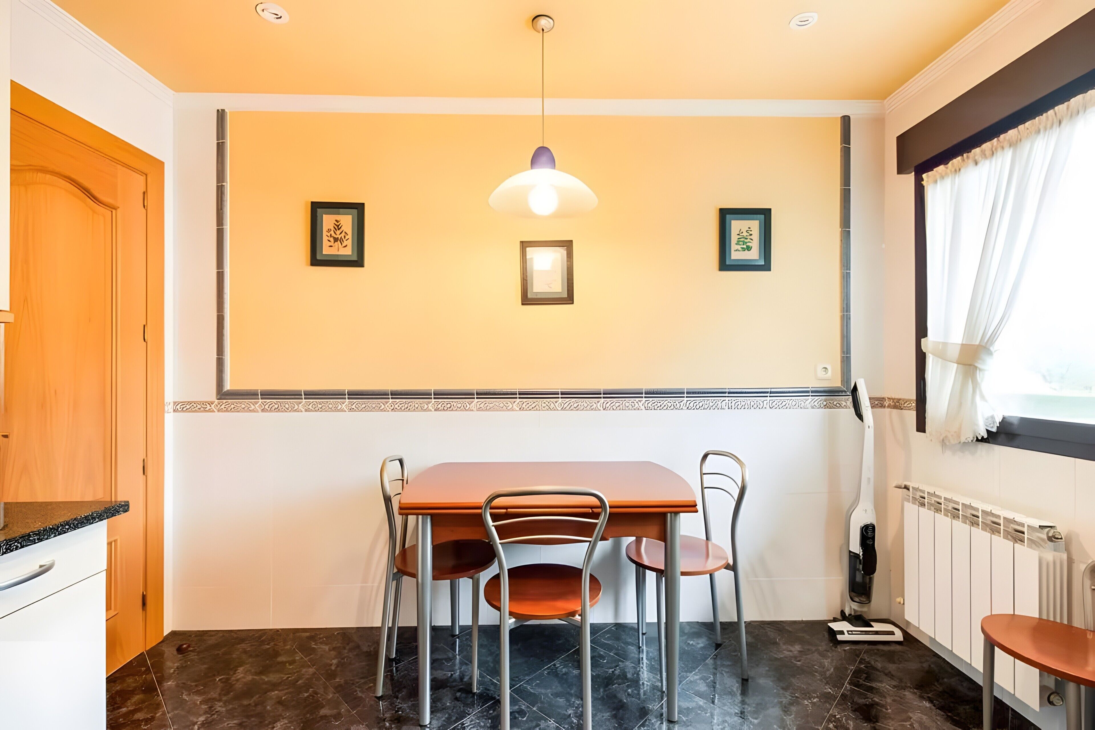 Un comedor con una mesa, sillas, una lámpara en el techo y cuadros en la pared.
