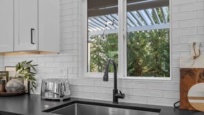 Una cocina moderna con armarios blancos, encimera negra, pileta de acero inoxidable y ventana con vista a follaje.