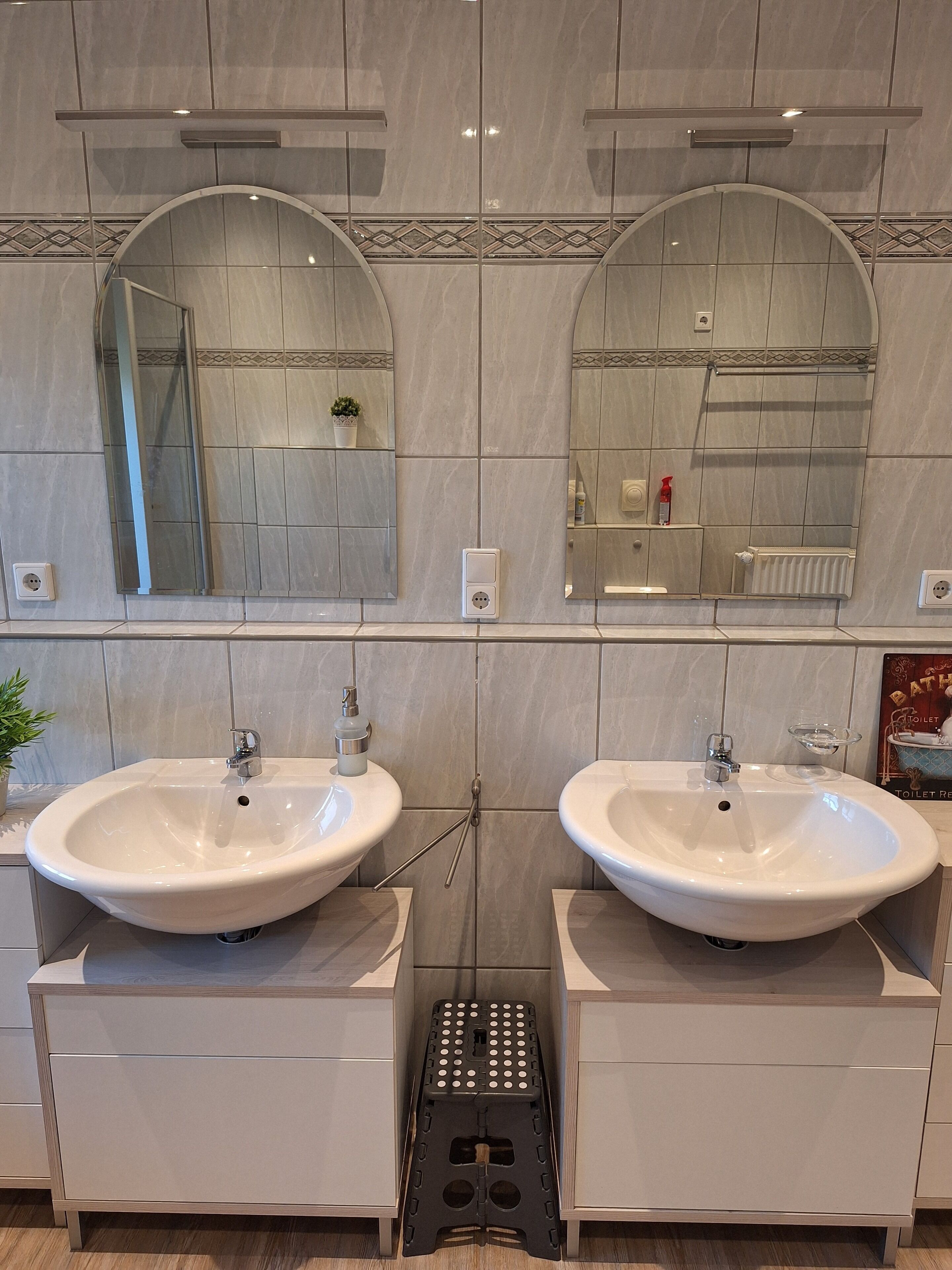 Ein Badezimmer mit zwei Waschbecken, einem Spiegel und einer kleinen Steh-Leiter.