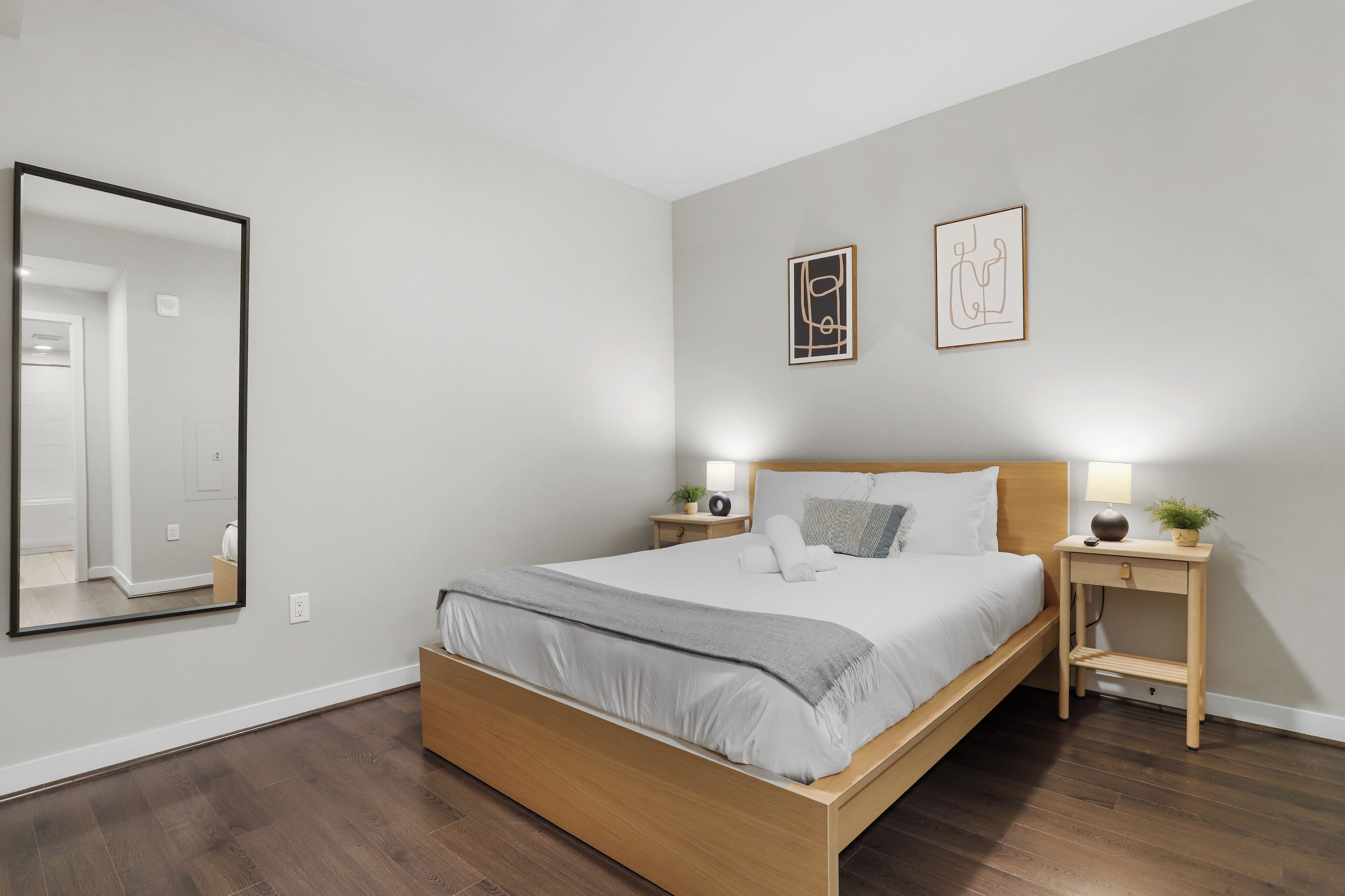 Un dormitorio moderno con una cama de madera, mesitas de noche con lámparas y obras de arte en las paredes.