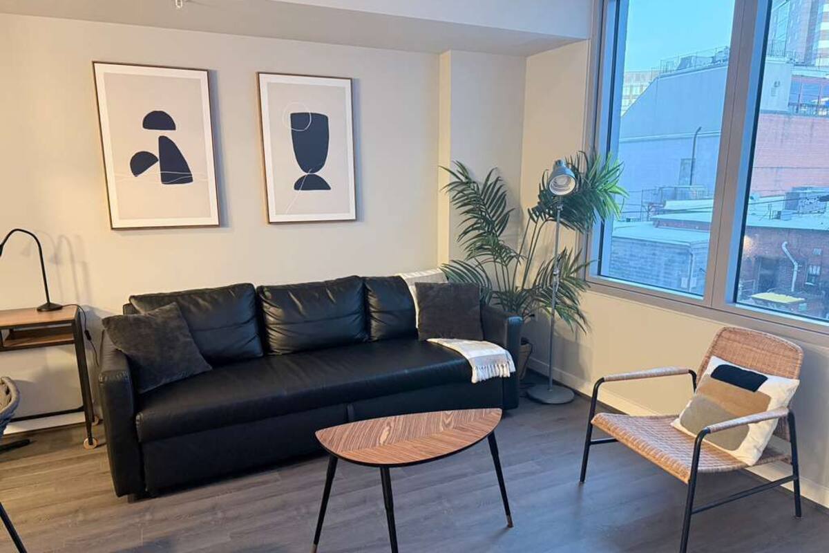 A modern living room with a black sofa, a wicker chair, a small wooden table, and two abstract paintings on the wall.