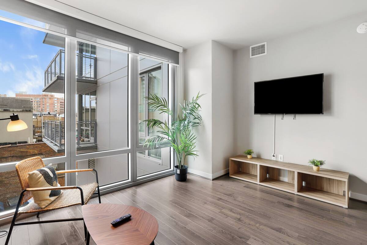 A modern living room with a large window, a flat-screen TV, a wooden bench, and a potted plant.