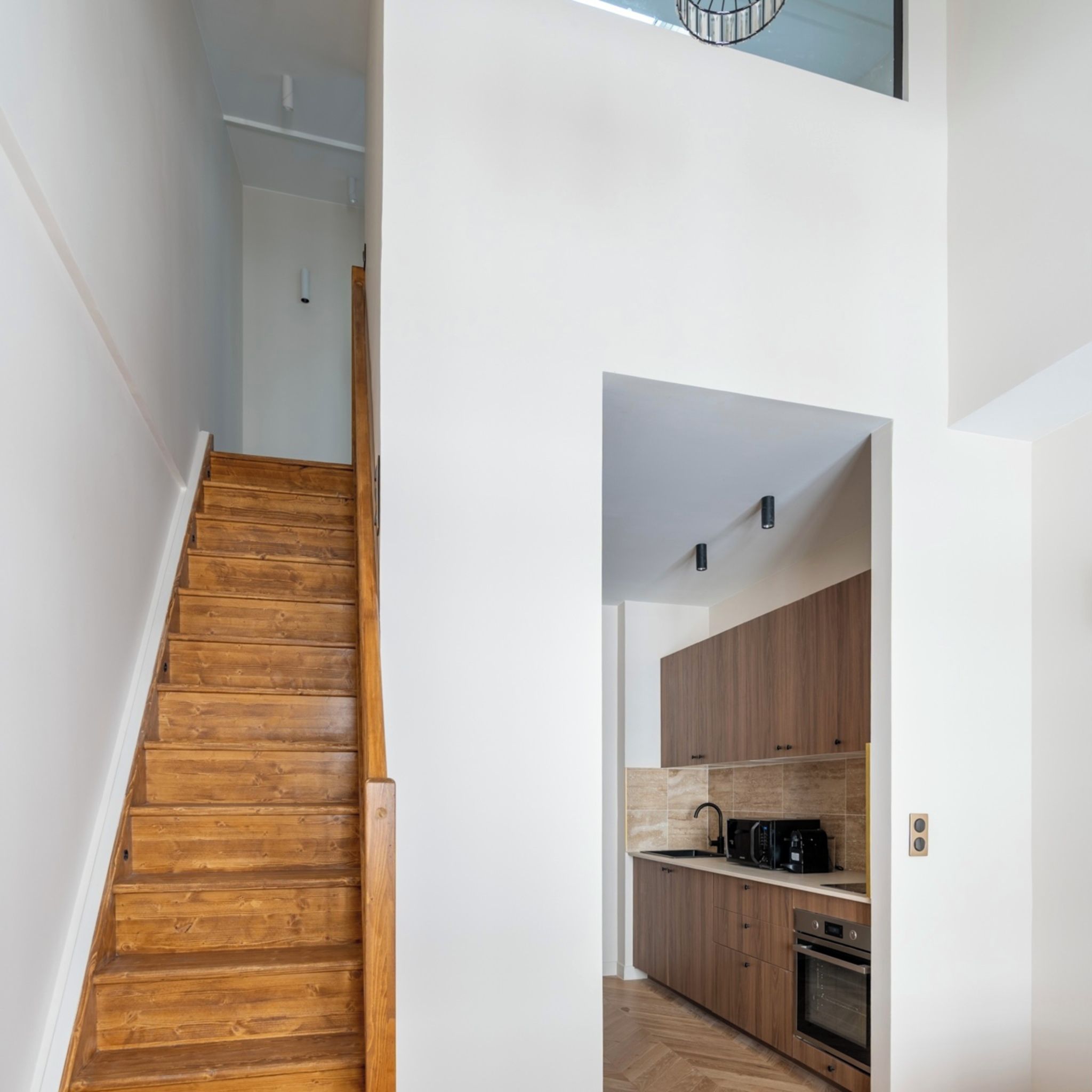 A wooden staircase leading to a kitchen with wooden cabinets and modern appliances.