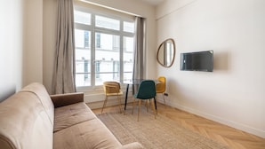 A modern living room with a sofa, a dining table with chairs, a flat-screen TV, and a large window with curtains. - Spacious Paris Duplex for 4 Near Bastille (Paris)