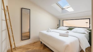 A bedroom with a skylight, a bed with white linens, a wooden ladder, and a mirror on the wall. - Spacious Paris Duplex for 4 Near Bastille (Paris)