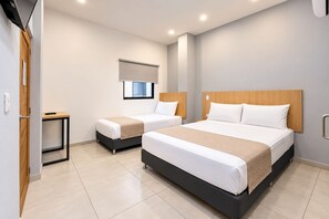 Une chambre d’hôtel avec deux lits, une petite table, une fenêtre avec un store et une porte avec une poignée.
