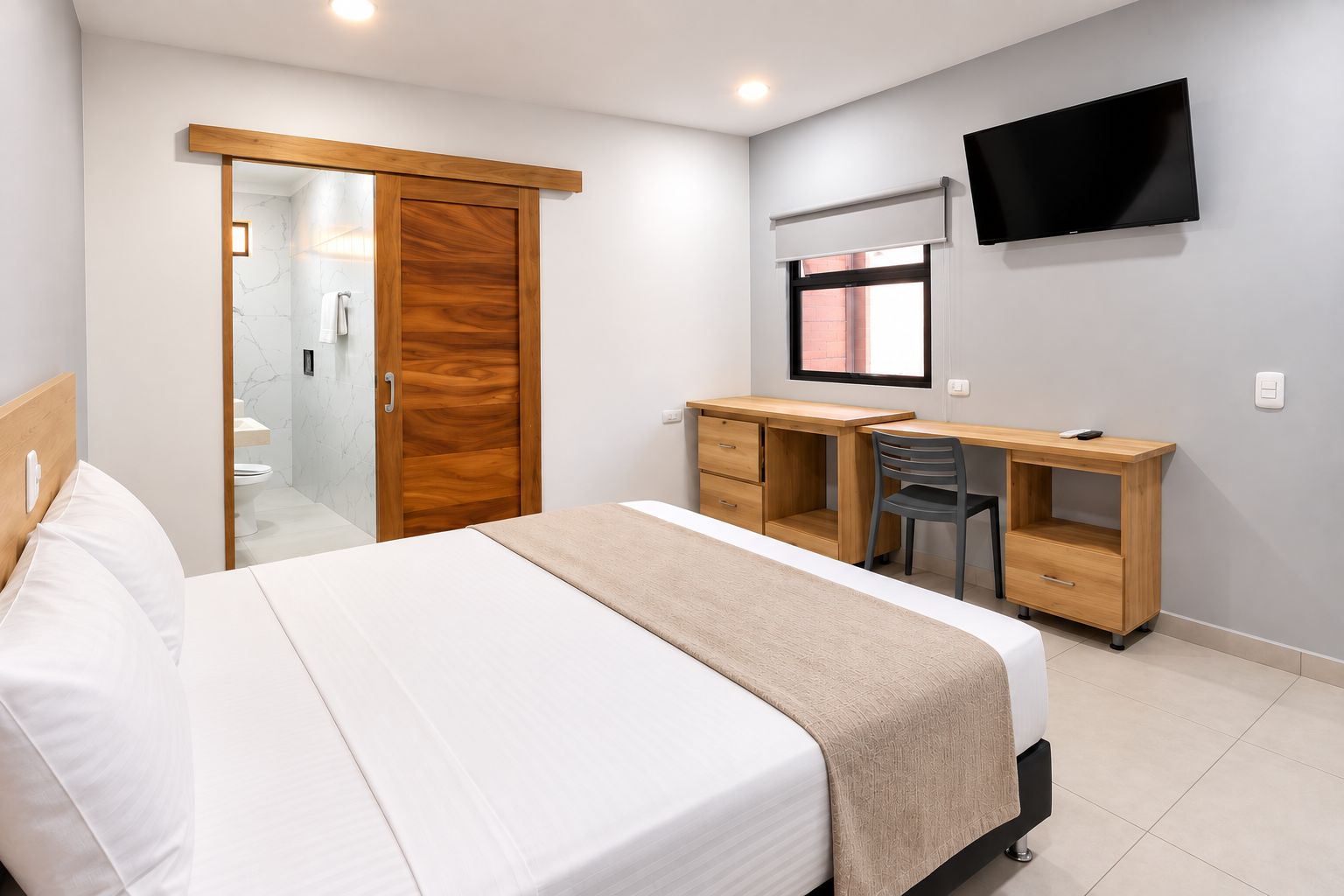 Habitación de hotel con cama, escritorio, silla, televisor y puerta corrediza al baño.