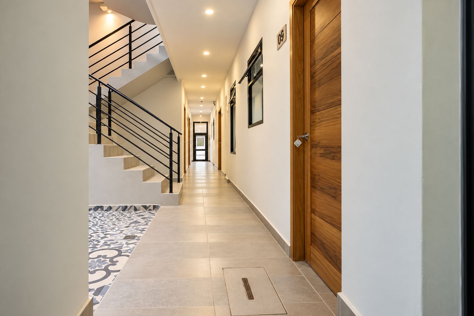A modern hallway with a staircase, a wooden door, and a tiled floor.