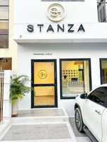Exterior de un hotel llamado STANZA, con un logo destacado, una entrada de doble puerta y un coche blanco estacionado.