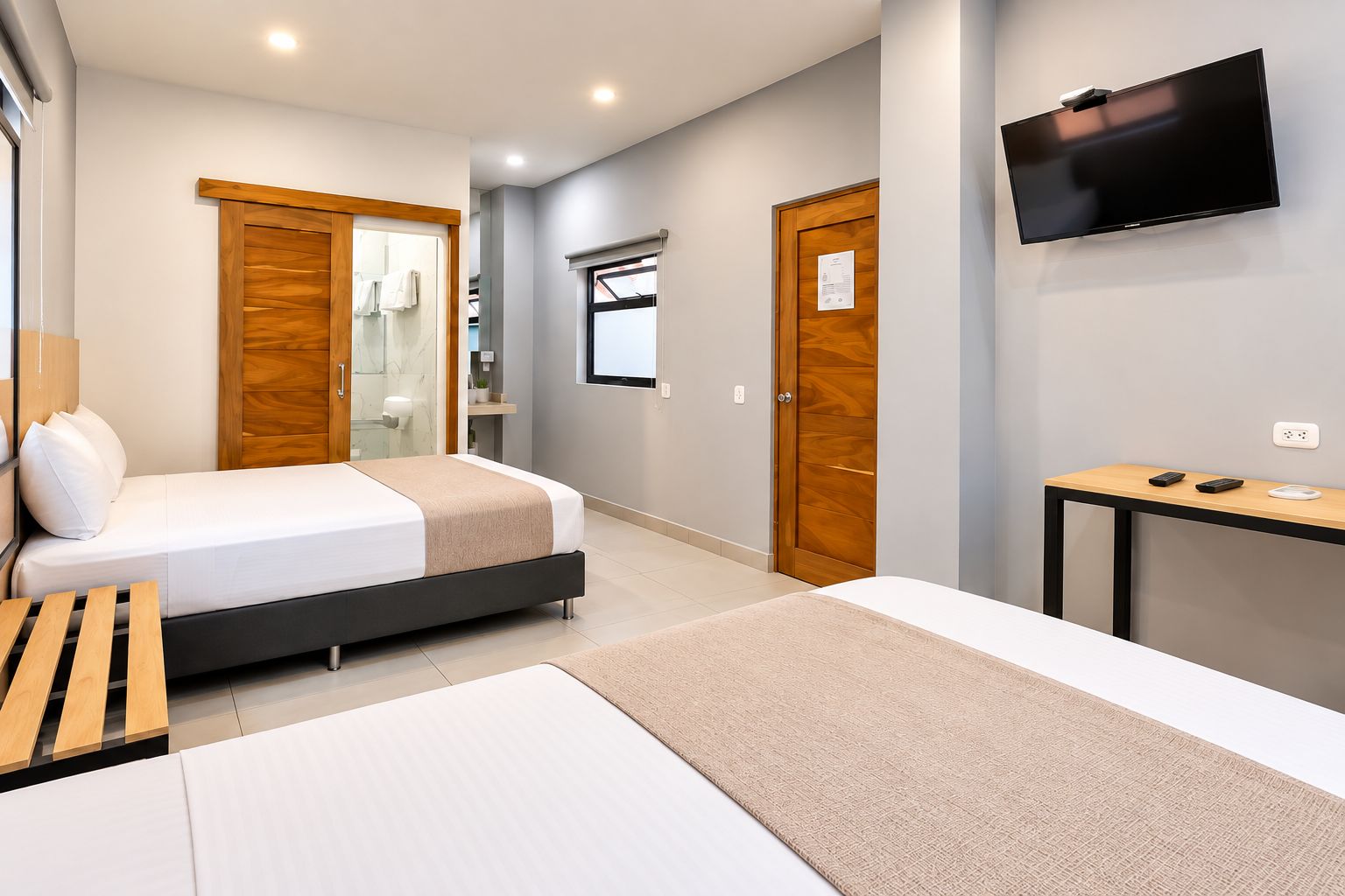 Ein Hotelzimmer mit Bett, Schreibtisch, Fernseher und einem durchgegangenen Tür sichtbaren Badezimmer.
