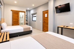 Une chambre d’hôtel avec un lit, un bureau, une télévision et une salle de bain visible à travers une porte ouverte.