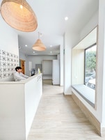 Zona de recepción de hotel con recepcionista, un mostrador de recepción, un ventanal con vistas al exterior y un pasillo que conduce a otras habitaciones.