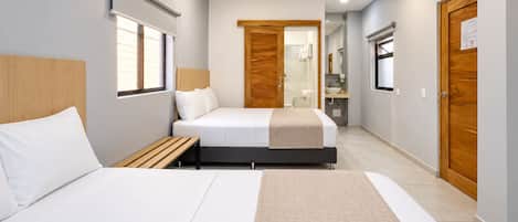 A hotel room with two beds, a wooden headboard, a bedside table, a bathroom with a mirror, and a wooden door.