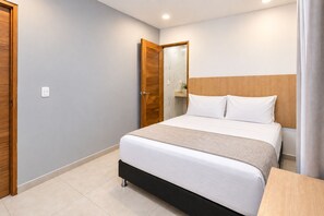 A modern bedroom with a bed, a wooden headboard, a nightstand, and a bathroom door. - Stanza Hotel Sincelejo (Sincelejo)