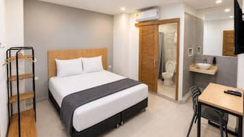 Habitación de hotel moderna con cama, escritorio, silla, armario, baño y televisor.