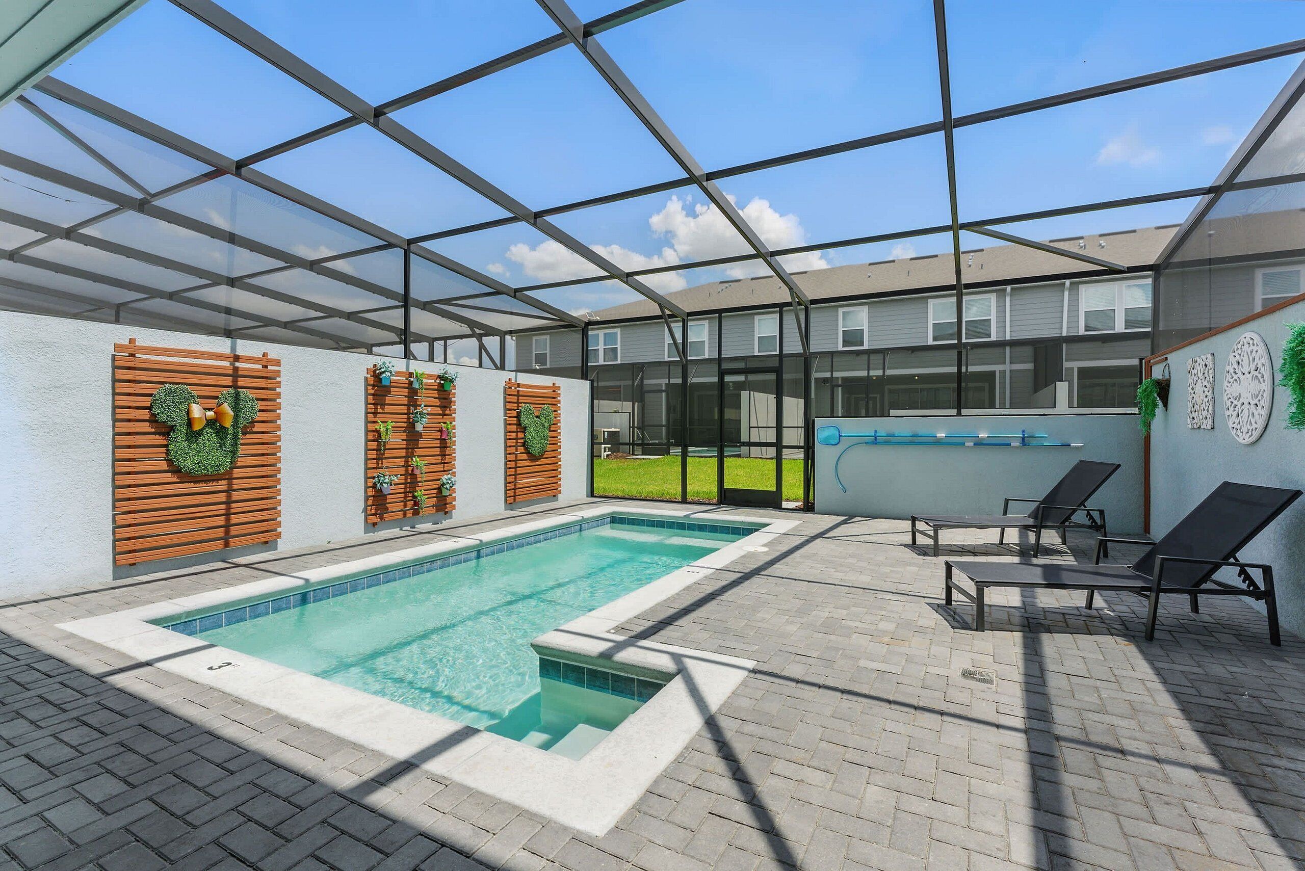 A covered swimming pool with lounge chairs, wooden panels, and decorative greenery.