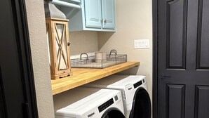 Un lavadero con dos lavadoras Whirlpool de carga frontal, un armario de madera con una cesta, y una puerta negra.