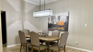 Un comedor con una mesa de madera y seis sillas tapizadas, una lámpara de araña y un cuadro con un paisaje urbano en la pared.